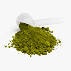 Green powder spilling out of a white scoop on a white background